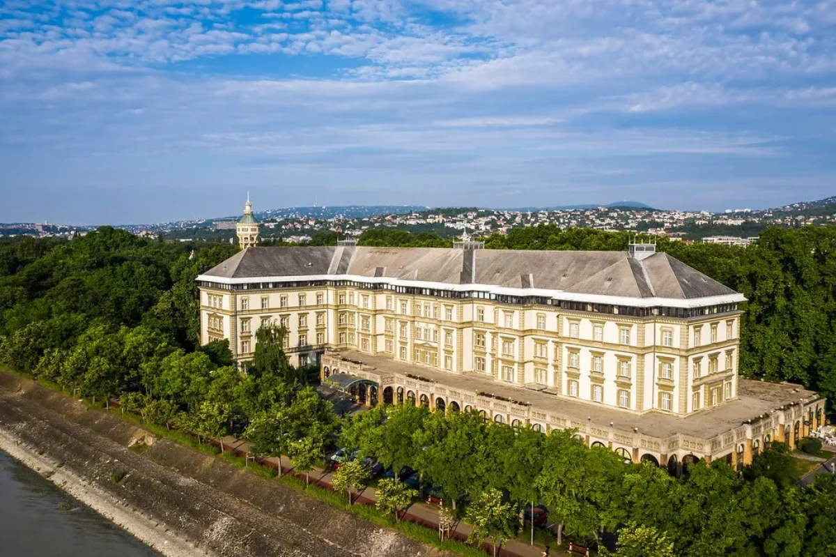Légi felvétel az Ensana Grand Margitszigetről, ahol a patinás krémszínű épület látható a Duna partján, erdők és Budapest panorámájával
