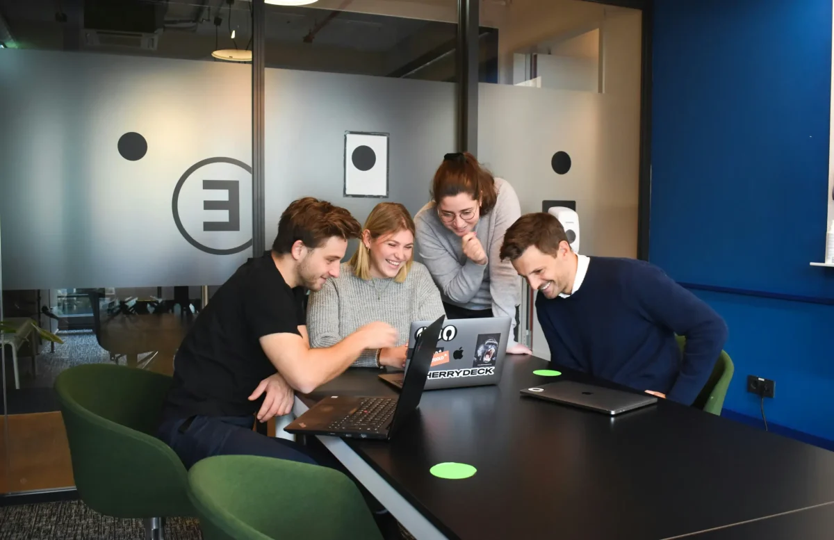 Fiatal csapat együttműködik laptopok előtt modern irodai meeting teremben mosolyogva